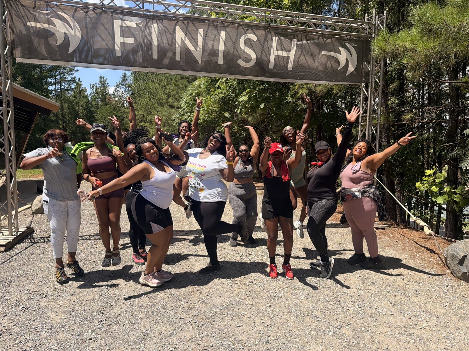A group of women cheering with arms raised beneath a FINISH banner outdoors