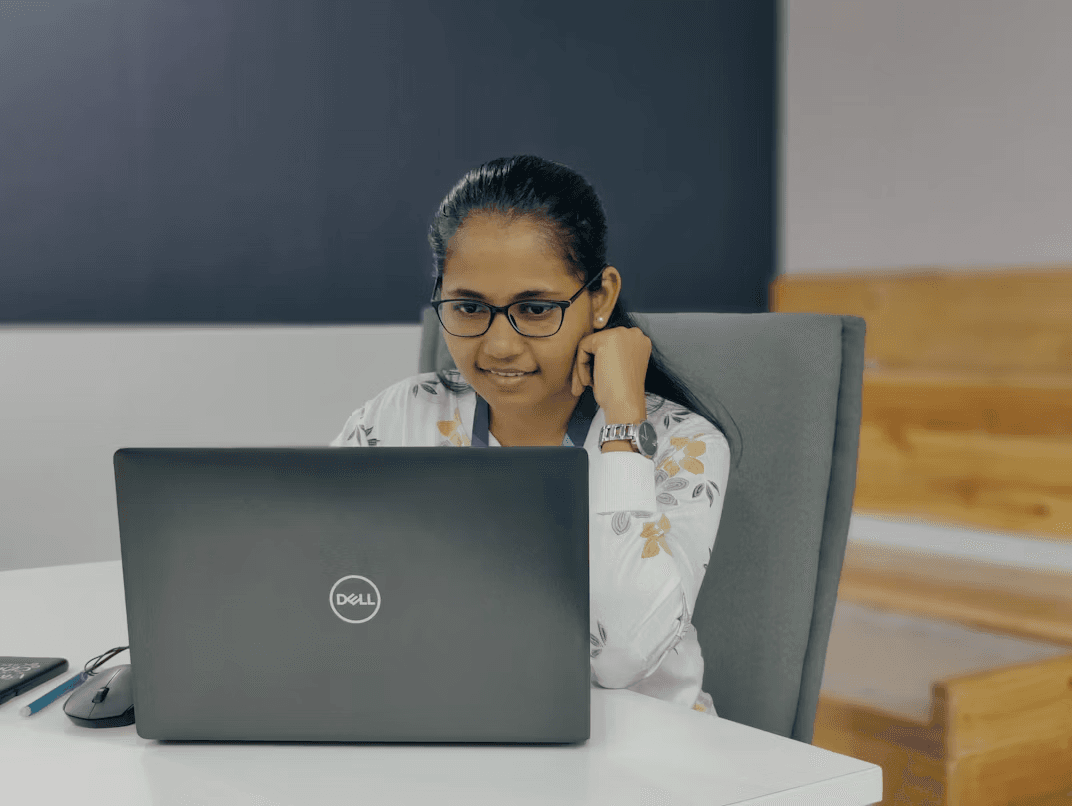 A woman at her desk, resting her chin on her hand as she looks at her laptop